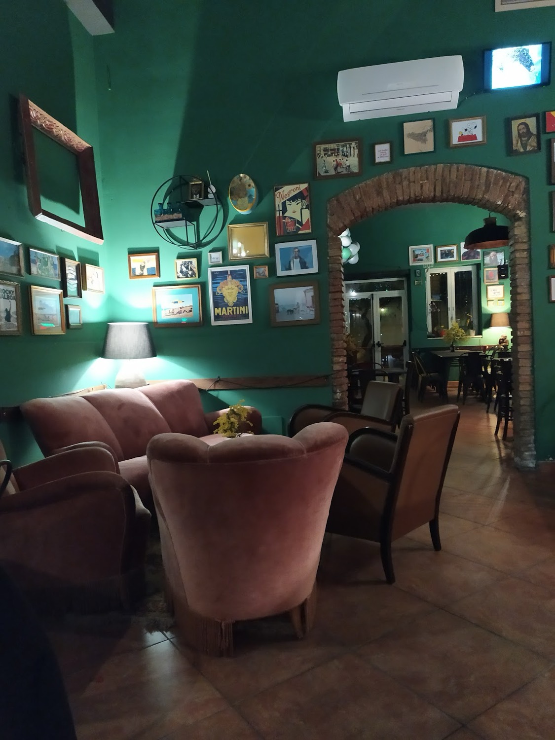 La sala della Taverna Meàri: pareti verde smeraldo, poltrone di velluto rosa, quadri incorniciati e un arco in mattoni